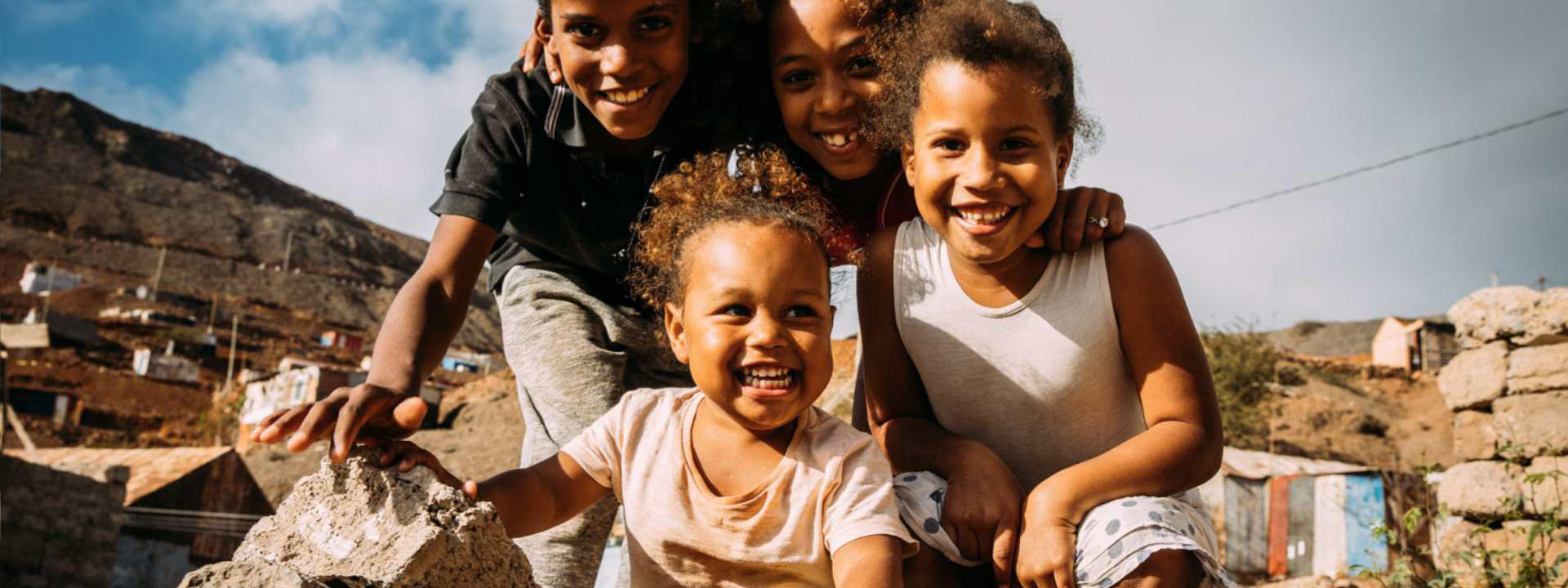 Vier Kinder sitzen im Freien auf Steinen und freuen sich über angekommene Spenden.